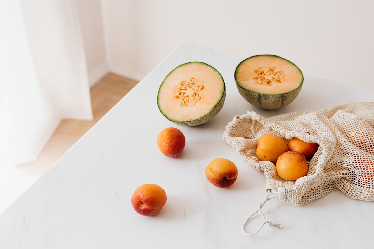 A melon cut in half and peaches on a white countertop