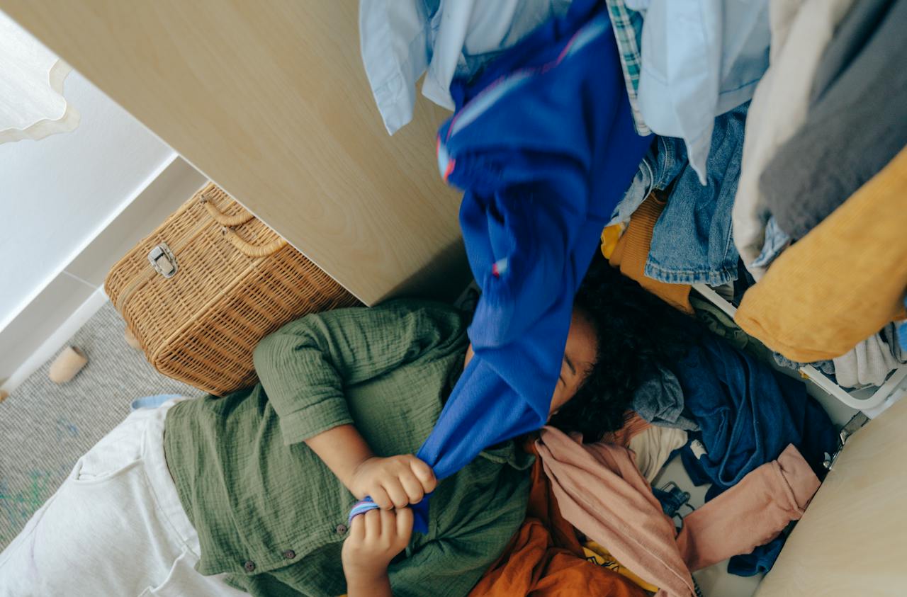 Girl lying on a stack of clothes in a bedroom.