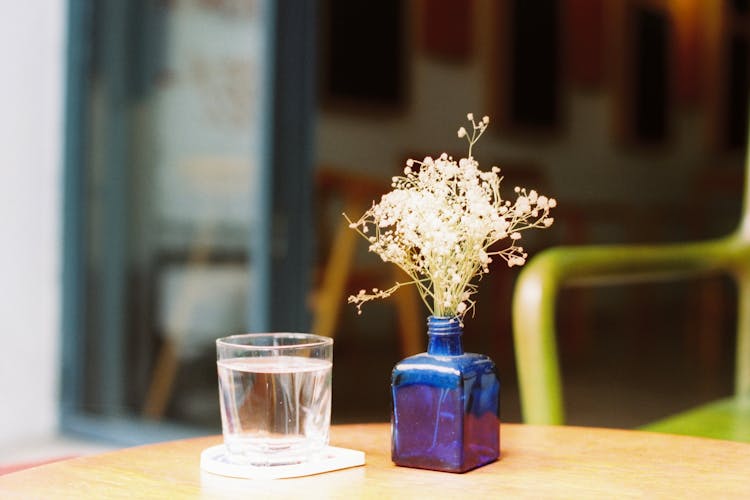 Small blue vase on the table and a glass of water next to it.