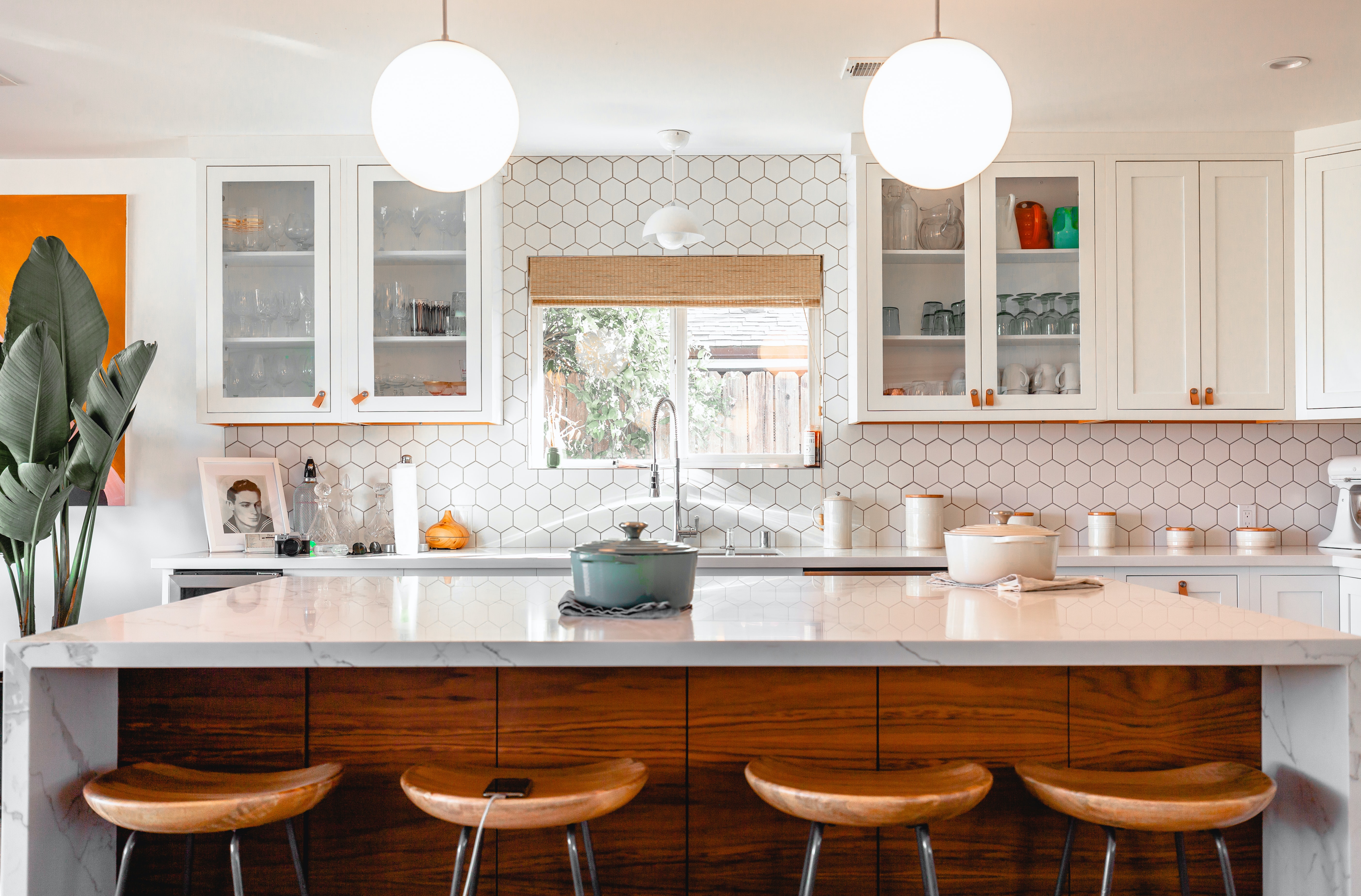 A kitchen island with brown chairs in a kitchen with white cabinets and a large plant in the right corner