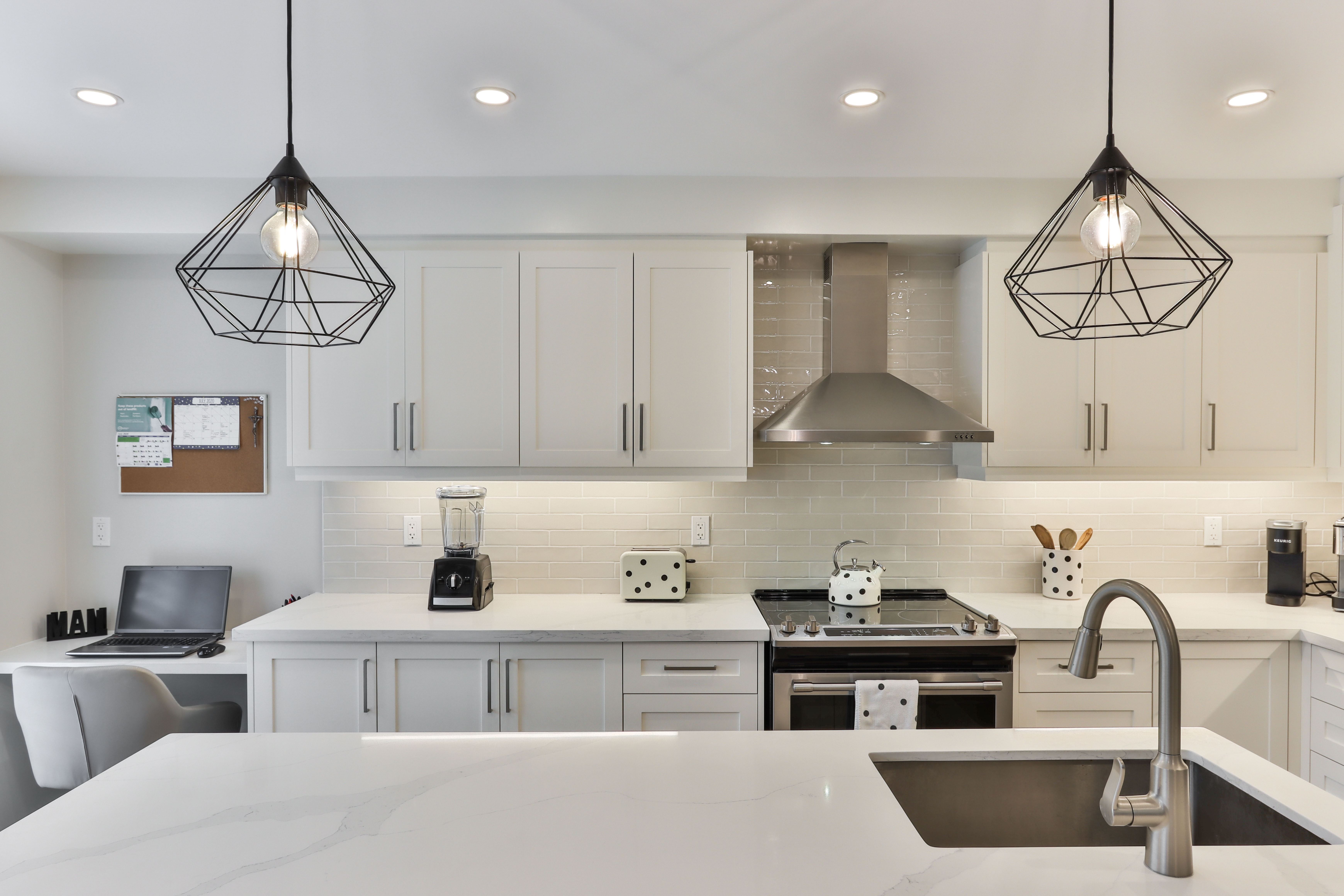 Two pendant lights in a bright kitchen with white countertops and white cabinets