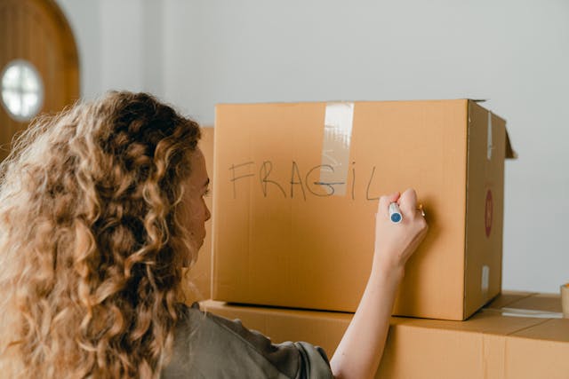 Curly-haired woman writing the word Fragile on a cardboard box